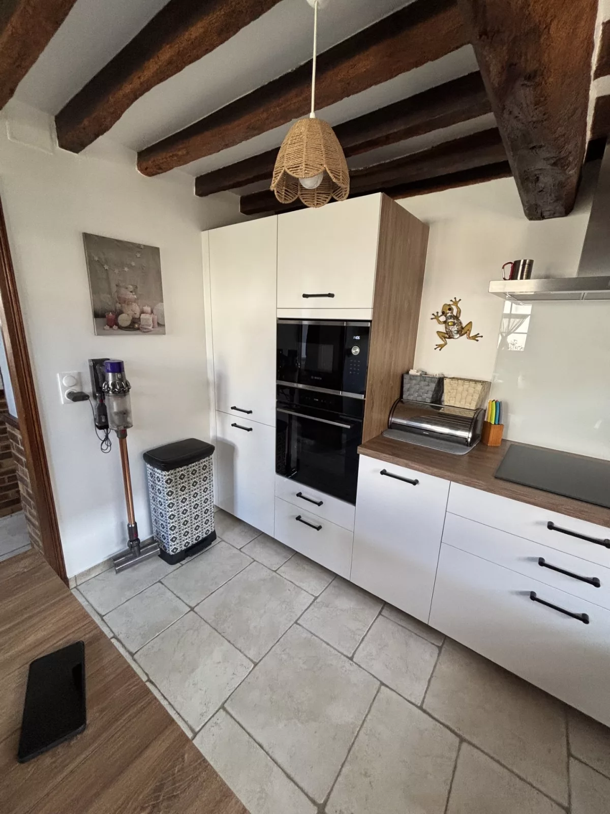 Mur technique avec l'armoire pour encastrement four et micro-ondes, le réfrigérateur et les meubles bas attenants surmontés d'un plan de travail en décor chêne de Fontainebleau.