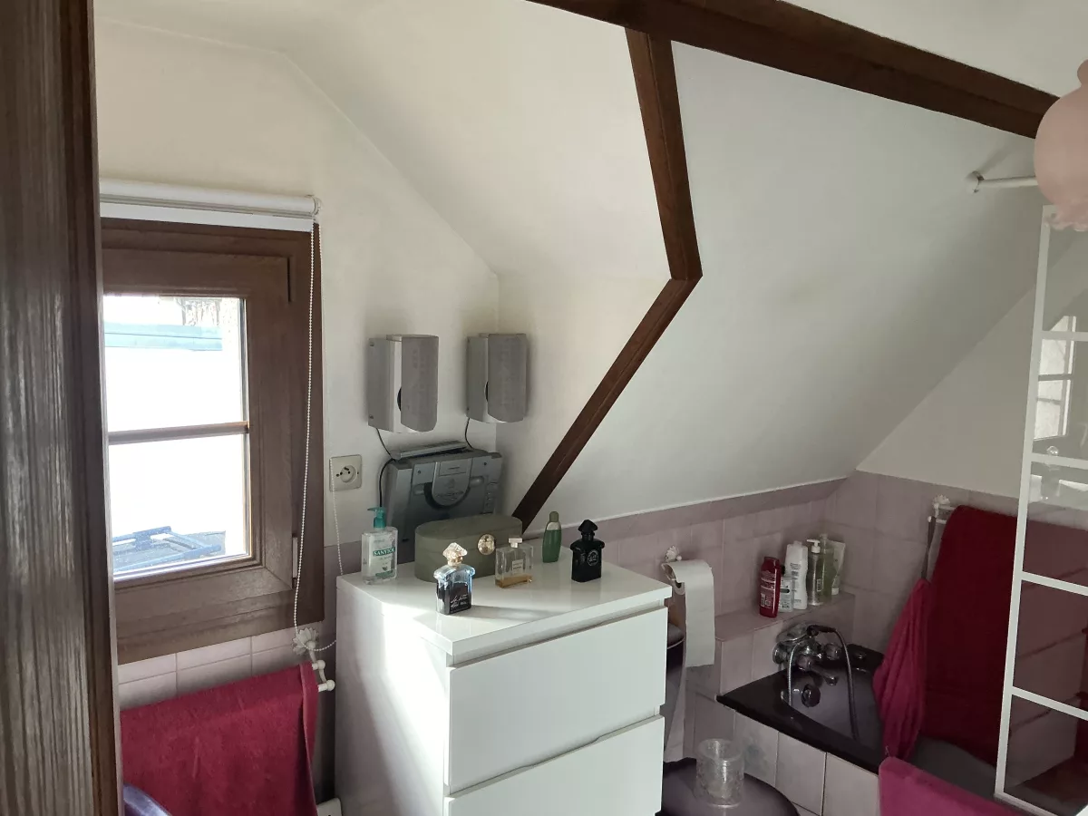 Vue avant travaux : autre angle de l'ancienne baignoire carrelée avec un meuble bas blanc à tiroirs.